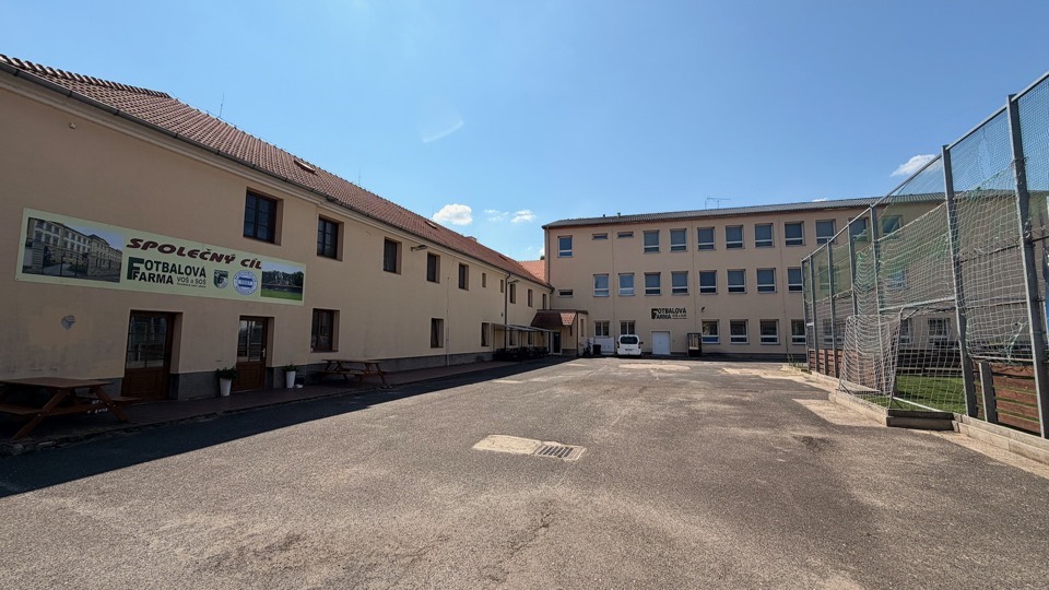 Dvůr areálu s parkovacím prostorem, starou i novou budovou a bannerem Společný cíl