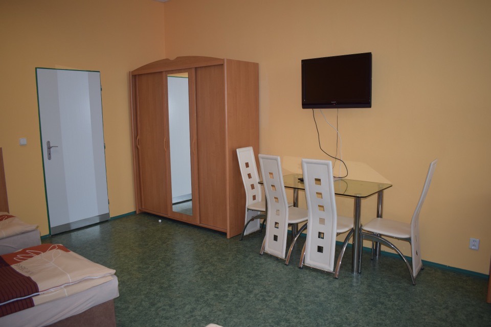 Apartmán se skříní, jídelním stolem a televizí na stěně