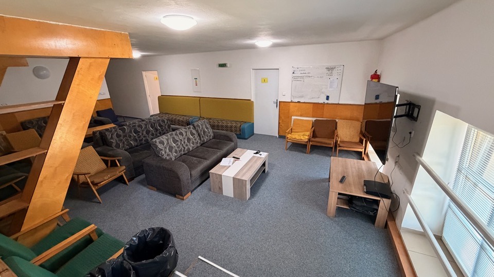 Společenská místnost staré budovy se sedačkami, křesly a televizí